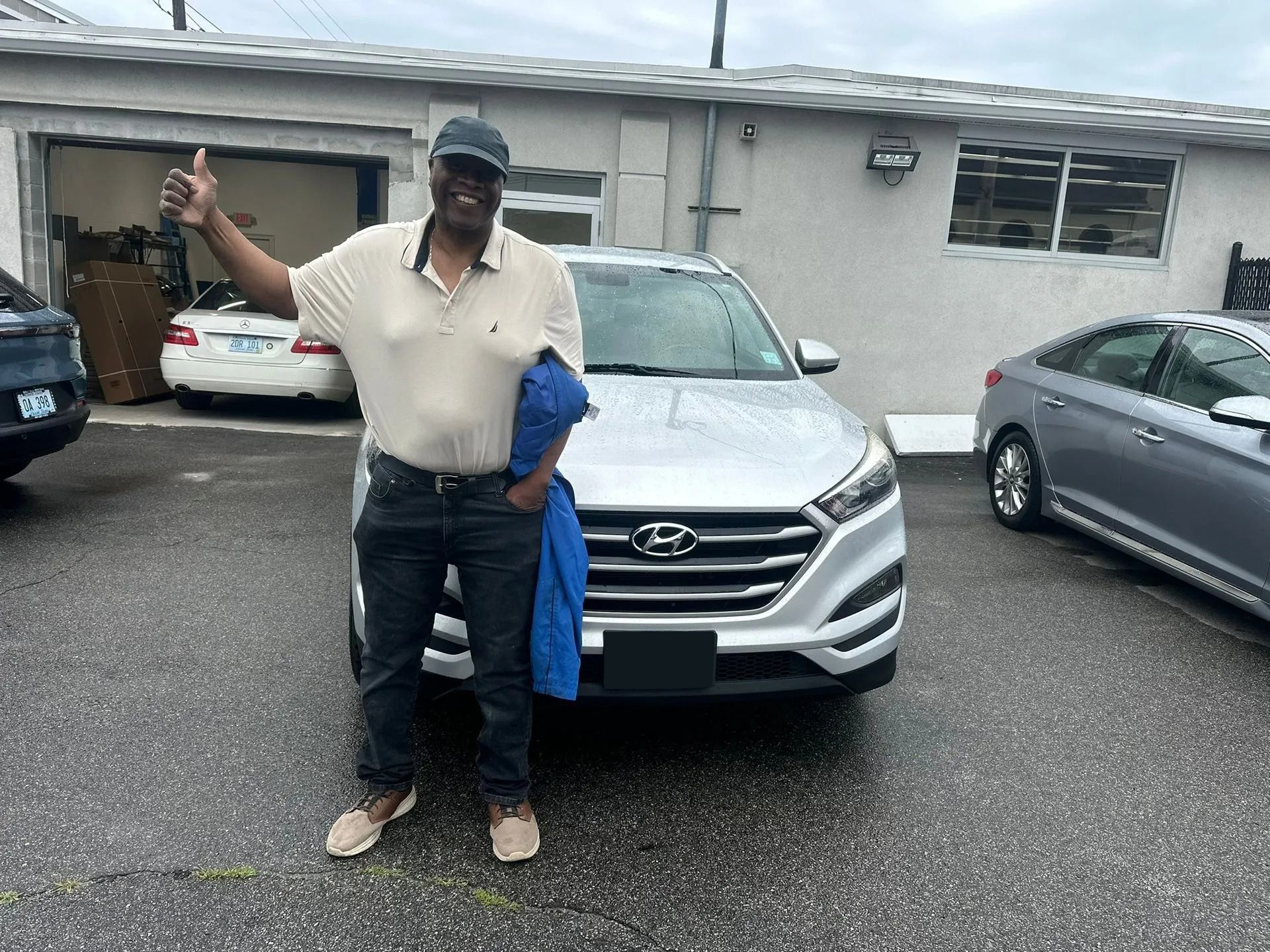 Man standing in a parking lot in front of a silver SUV, holding a blue cloth and raising one arm.