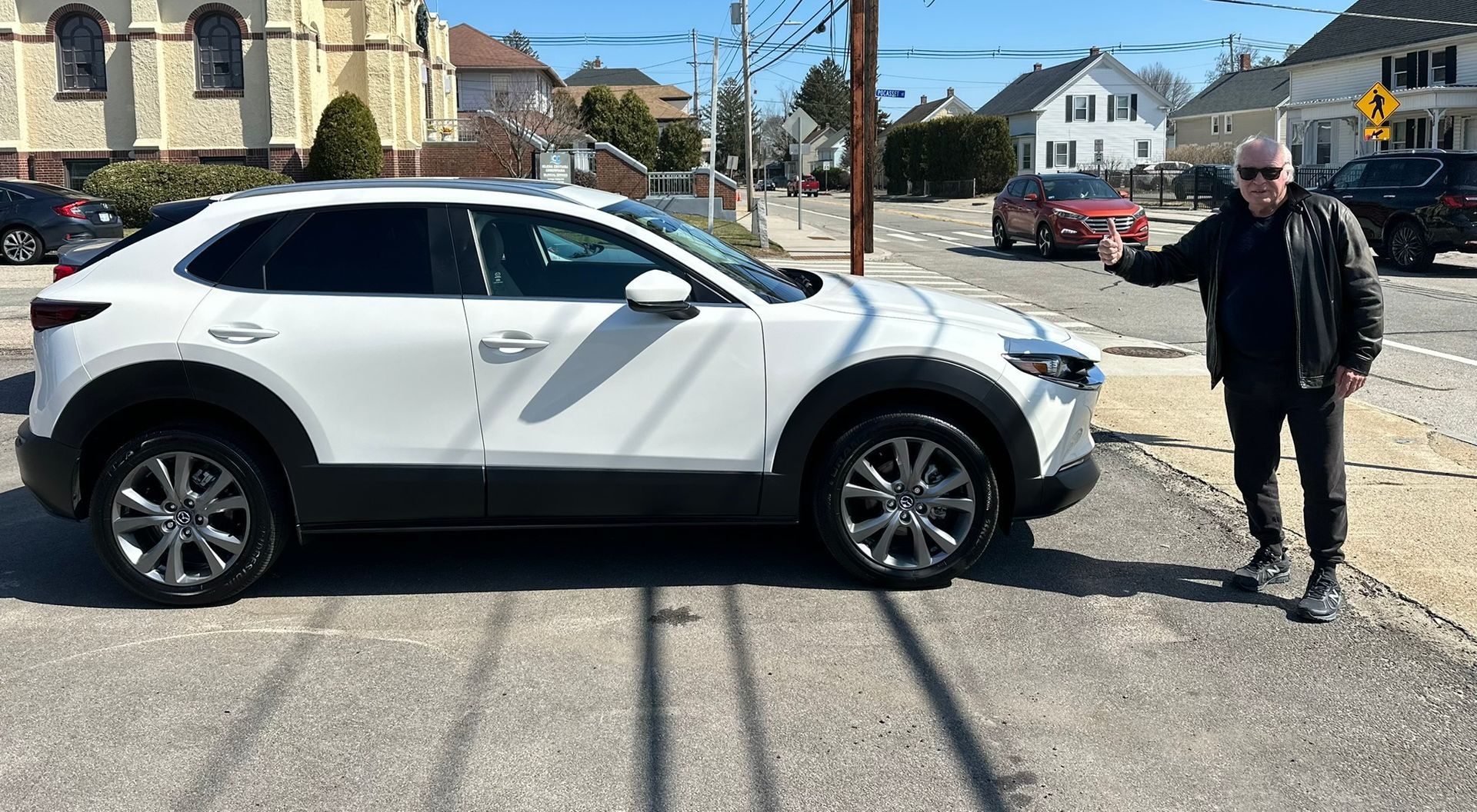 White SUV parked on a street with a man standing beside it in a sunny residential area
