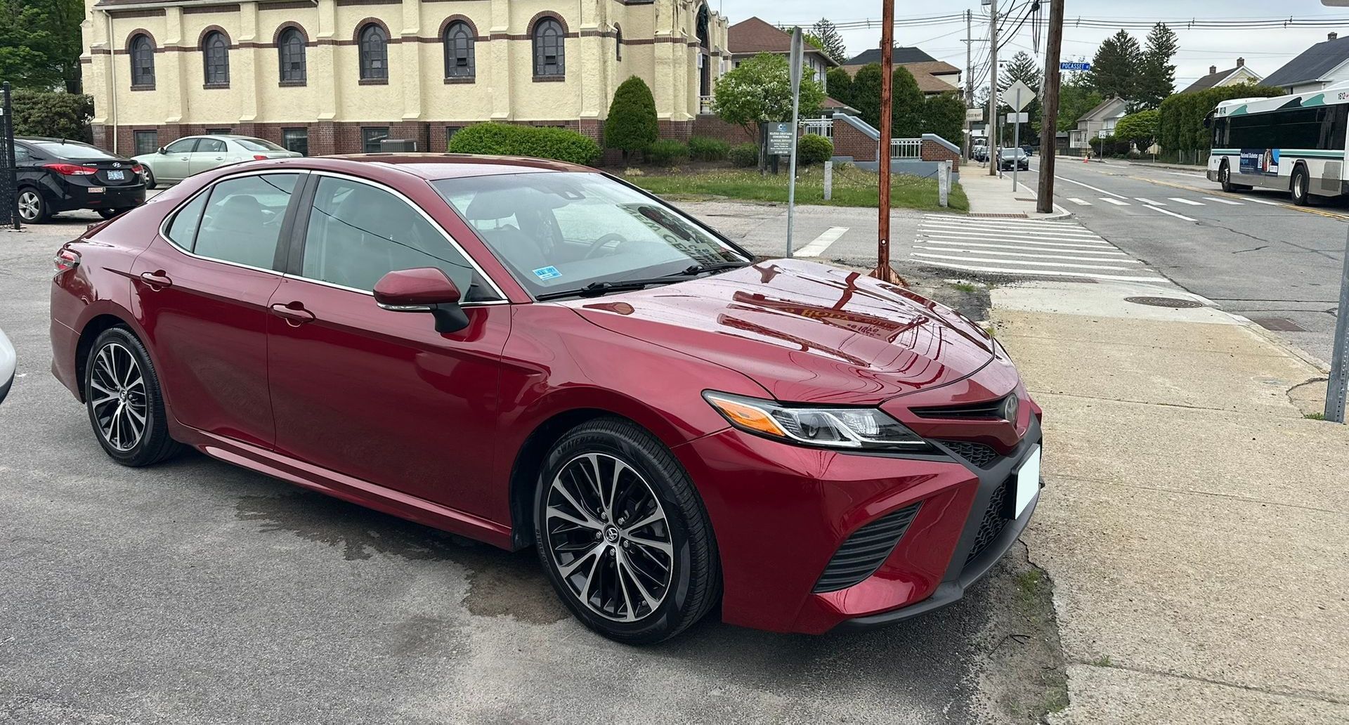 Red sedan parked at a curb on a cloudy street corner.