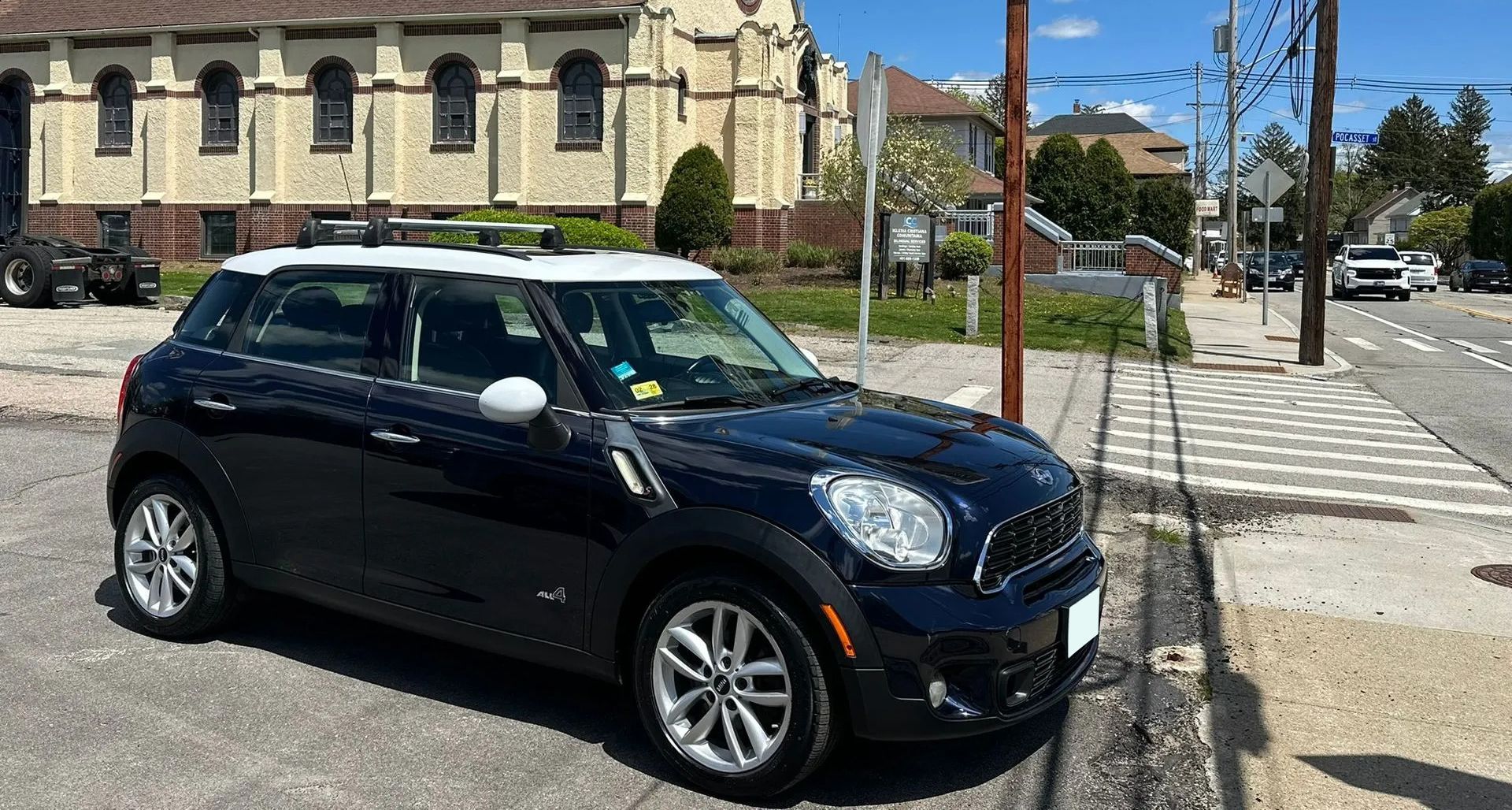 Black compact SUV parked on a sunny city street beside a stone building and crosswalk.