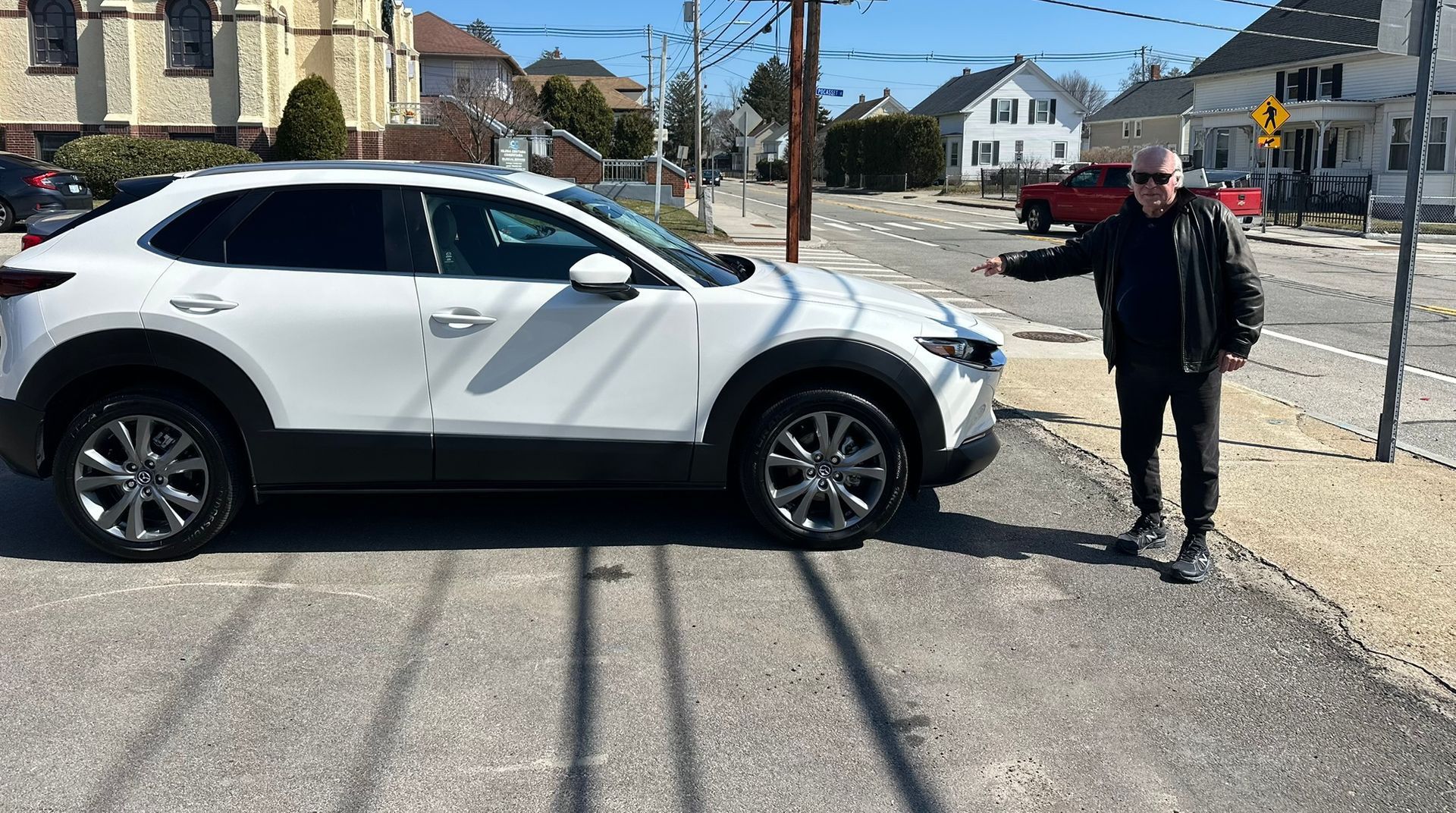 Person standing beside a white SUV on a sunny residential street.
