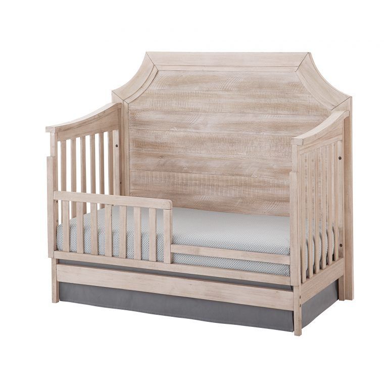 a wooden Remi clip crib with a toddler railing and a mattress