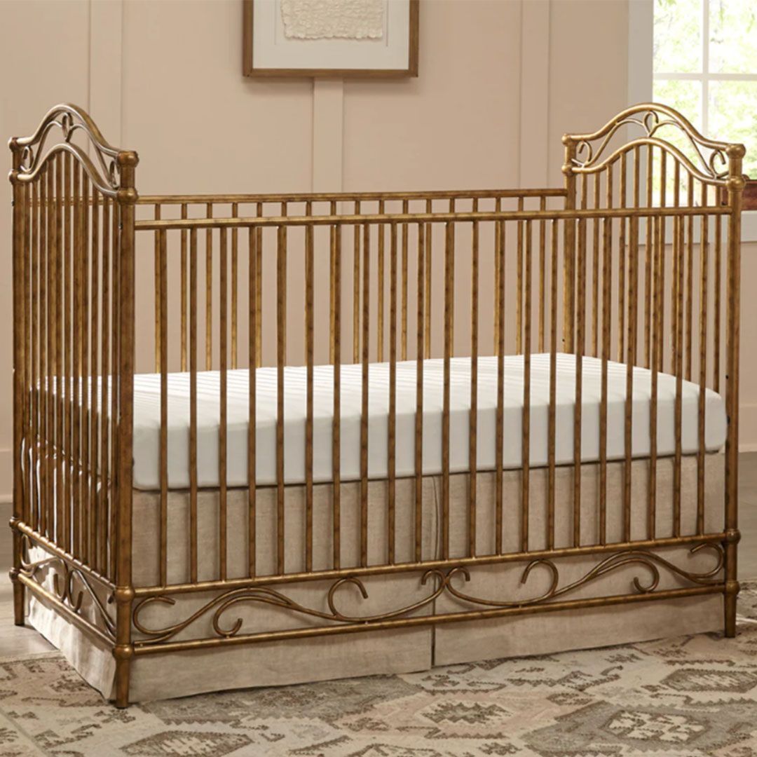 A gold crib with a white mattress is sitting on a rug in a room.