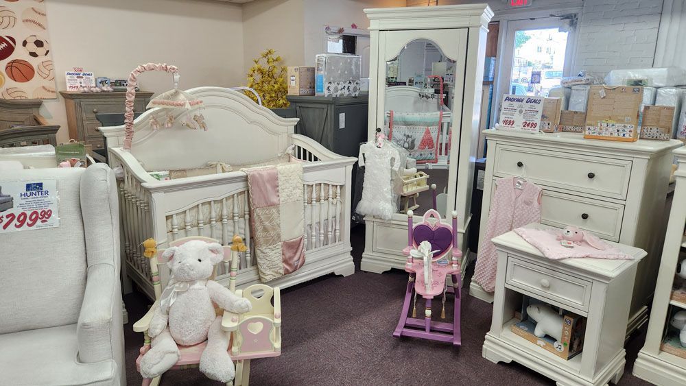 A baby room with a crib, rocking chair, nightstand, dresser and mirror