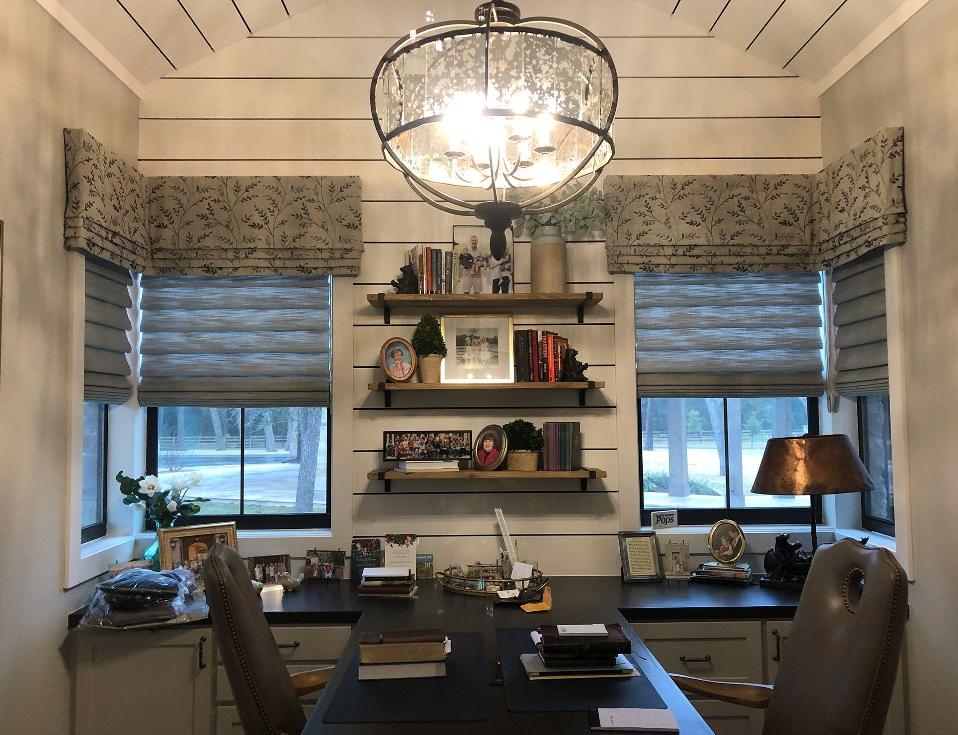 A home office with a desk , chairs , shelves and a chandelier.