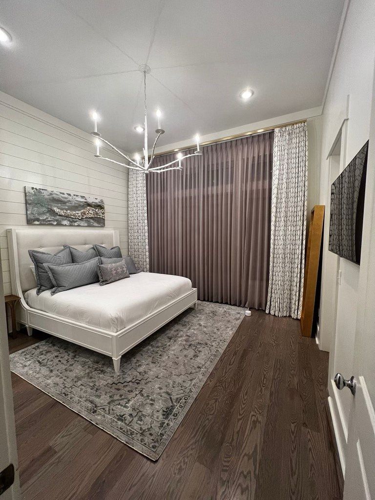 A bedroom with a large bed , rug , curtains and a chandelier.