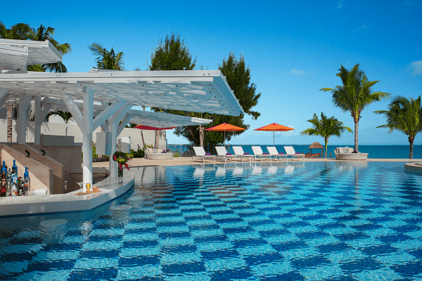 Poolside bar overlooking a checkered pool with lounge chairs and ocean view under a blue sky.