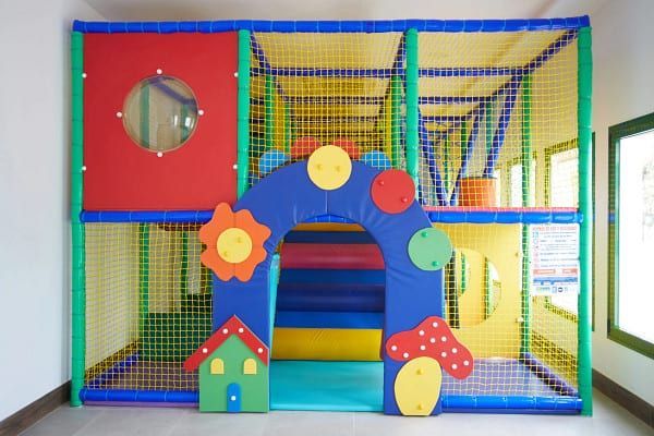 Colorful indoor playground with netting, tunnels, and soft play structures.