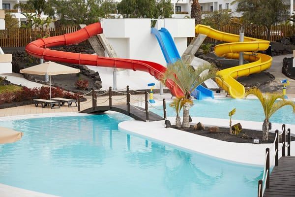 Water park with red, blue, and yellow water slides emptying into a pool; black bridge.