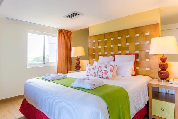 Hotel bedroom with a king-sized bed, two lamps, a window, and a nightstand.