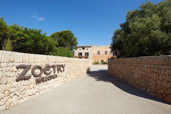 Zoëtry Mallorca hotel entrance sign on a stone wall, blue sky, trees.