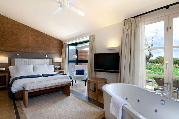 Luxury hotel suite with bed, bathtub, and outdoor view.