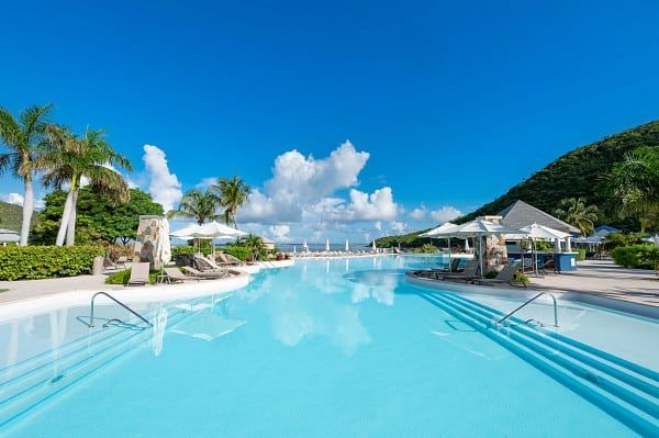 Blue swimming pool with lounge chairs and bar, against a backdrop of green hills and blue sky.