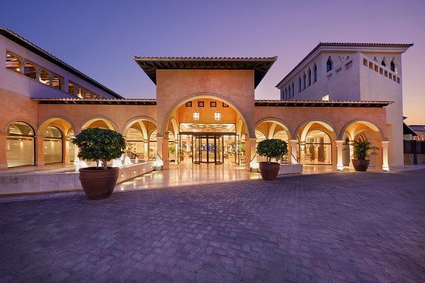 Hotel entrance at dusk, featuring arched doorways, terracotta facade, and potted plants.
