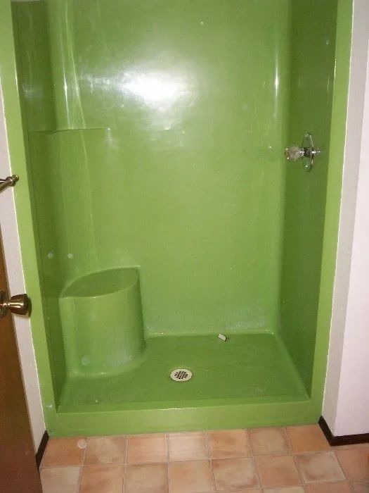 a green shower stall with a seat in a bathroom