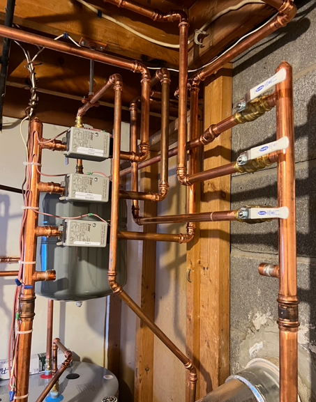 Copper pipes and water meter in an unfinished utility room with exposed concrete walls.