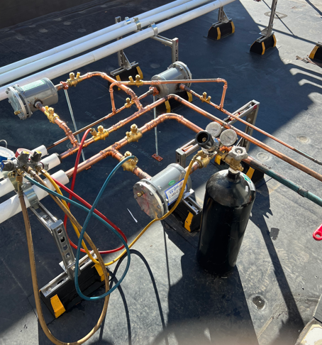 Copper pipe and gas cylinder setup on a rooftop, with hoses and metal fittings