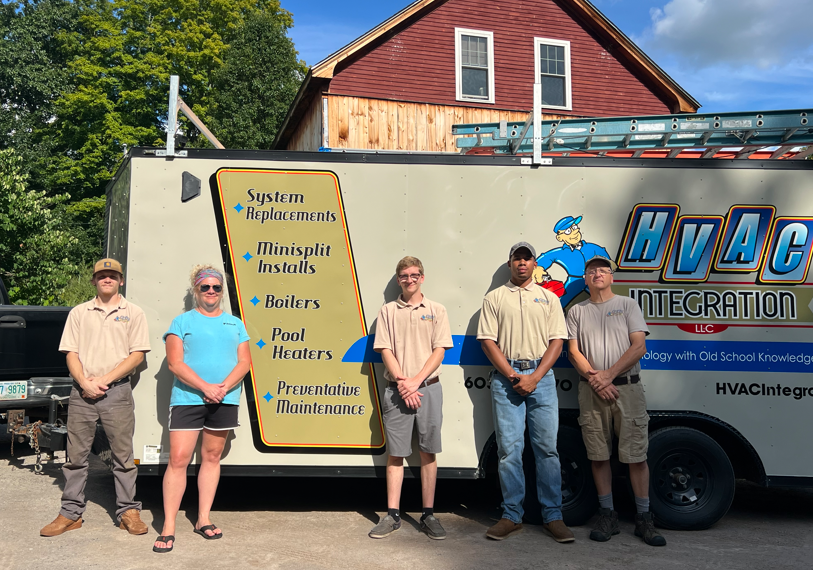 HVAC technician team posing beside a service truck and a signboard outside a house