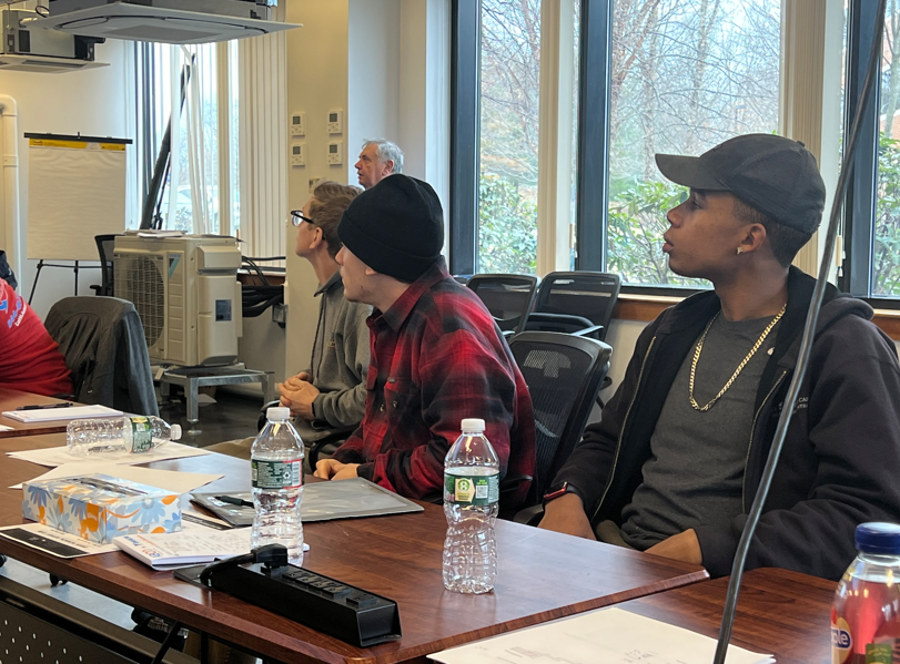 People seated at a conference table in a bright meeting room, listening attentively.