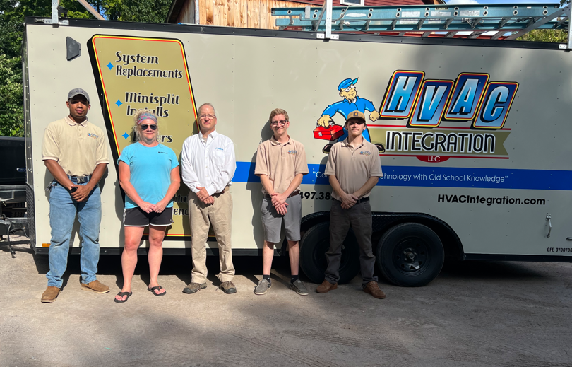 Five people stand beside a HvAC Integration service truck in bright sunlight.