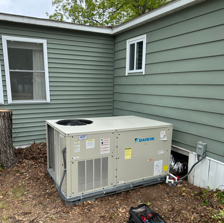 Outdoor HVAC unit beside a green house wall and white-trimmed windows
