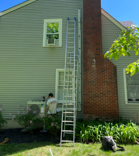 Person on a ladder working beside a brick chimney on a house exterior