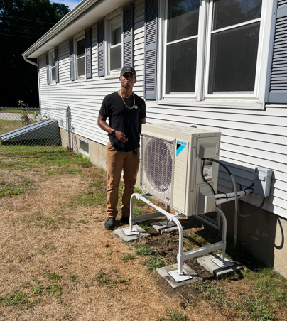 Person standing beside an outdoor air conditioner unit on a house exterior.