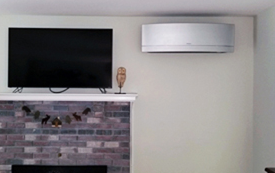 Wall-mounted TV above a brick fireplace with a white air conditioner on a beige wall.