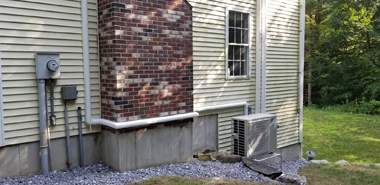Side of a house with utility meter, brick and siding, and an outdoor air conditioner unit on gravel.