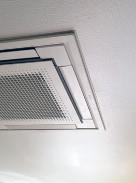 Ceiling-mounted white air vent with a perforated panel against a white ceiling.