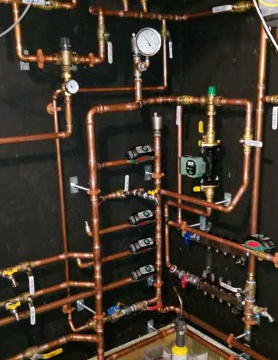 Copper plumbing manifold with gauges, valves, and pipes installed in a utility room.