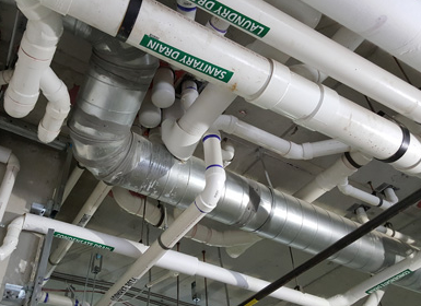 Ceiling view of white PVC and silver HVAC ducts and pipes in an industrial utility space
