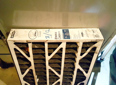 White HVAC air filter leaning against a vent, with dust visible on the frame and grille.