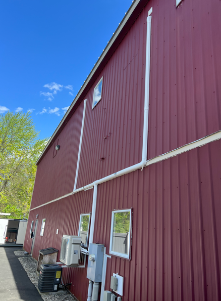 Red barn with white trim and several utility boxes on the exterior wall under a blue sky.