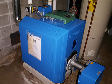 Blue boiler unit in a basement, connected to ducts and pipes with a small blue pump attached.