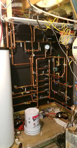 Partially completed plumbing and wiring in a utility room with copper pipes and black wall panels