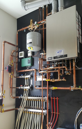 Wall-mounted boiler and water heater with copper pipes and valves in a utility room.
