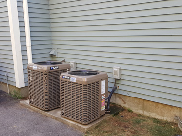 Two outdoor air conditioning units beside a house with light blue siding.