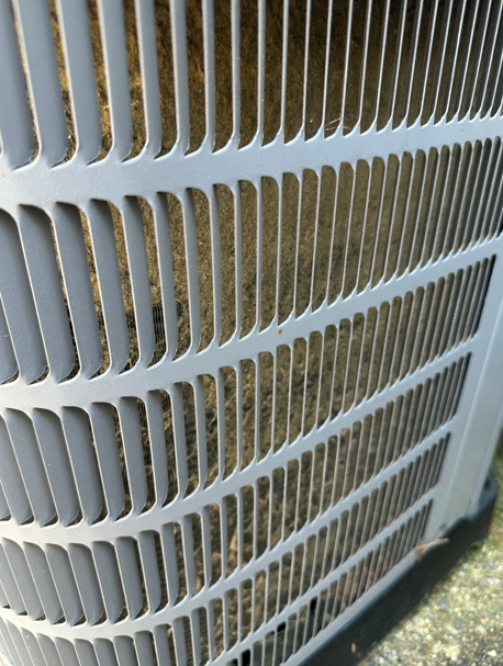 Close-up of a white air conditioner condenser grille outdoors, with curved vent slats.