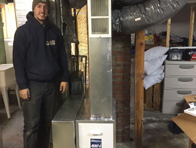 Man standing beside a metal HVAC duct in a basement utility room