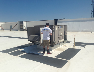 Worker inspecting rooftop HVAC unit on a flat white roof in bright sunlight.