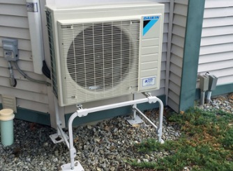 Outdoor air conditioner unit beside a house, with white piping on a gravel bed.