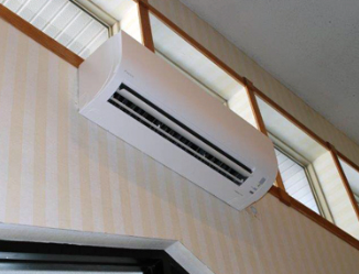 White wall-mounted air conditioner above a doorway in a room with striped wallpaper and high windows