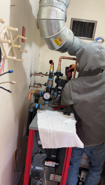 Person in a gray hoodie working on a red cart with pipes and gauges in a utility room.