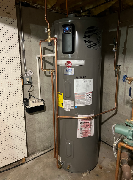 Gray water heater in a basement utility room with copper pipes and gauges.