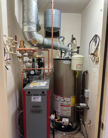 Utility closet with a furnace, water heater, and exposed pipes and ductwork.