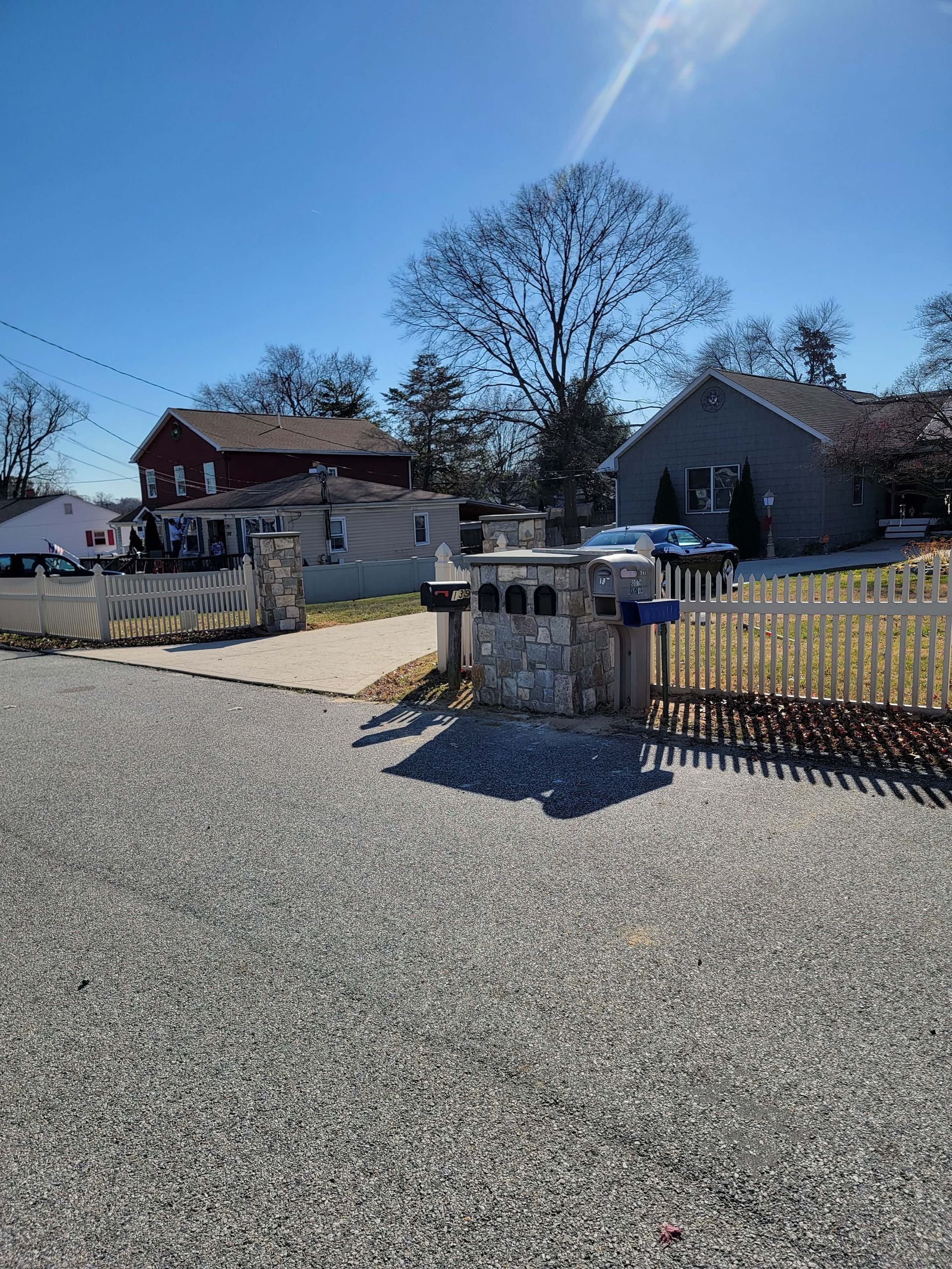 a gravel driveway leading to a house with a fence and mailboxes