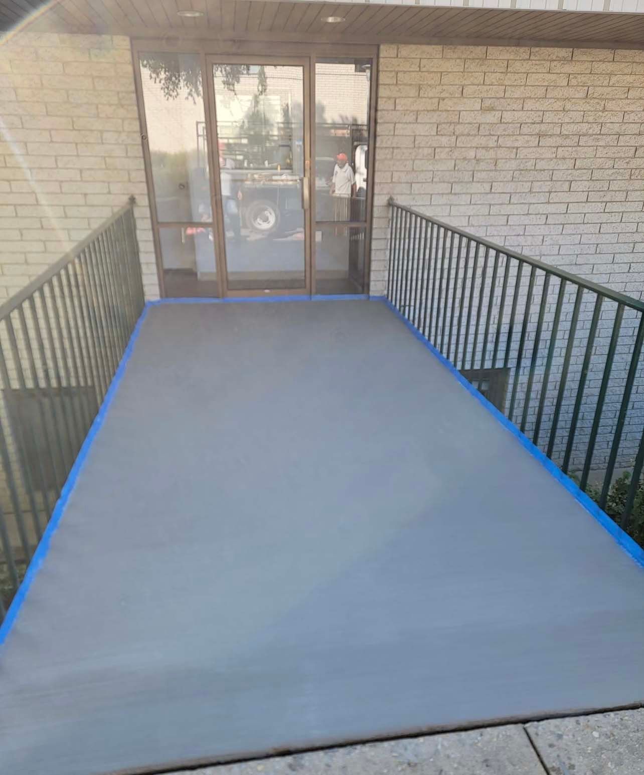 a concrete walkway leading to a building with a railing and a door .