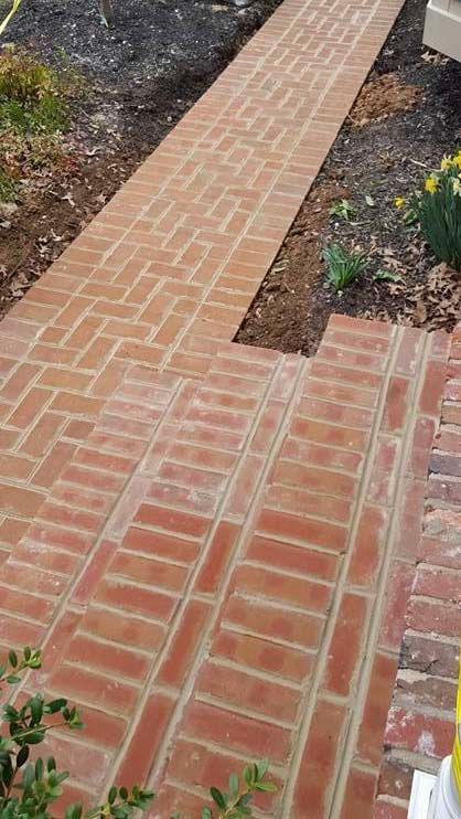 a brick walkway leading to a house with flowers in the background .