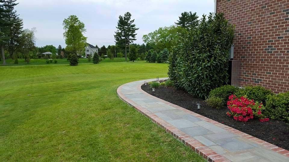 a walkway leading to a brick house with a lush green field in the background .